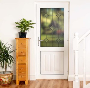 white entrance door with leaded glass pane beside wooden furniture unit, staircase and potted plants