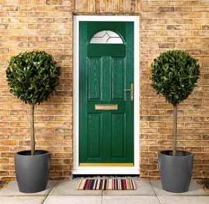 green entrance door with brick wall, welcome mat and potted trees