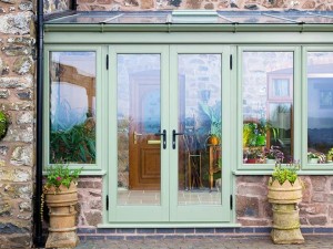 Light green timber conservatory with french doors and stone walls
