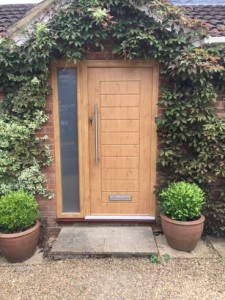 Light brown wooden front door framed by greenery